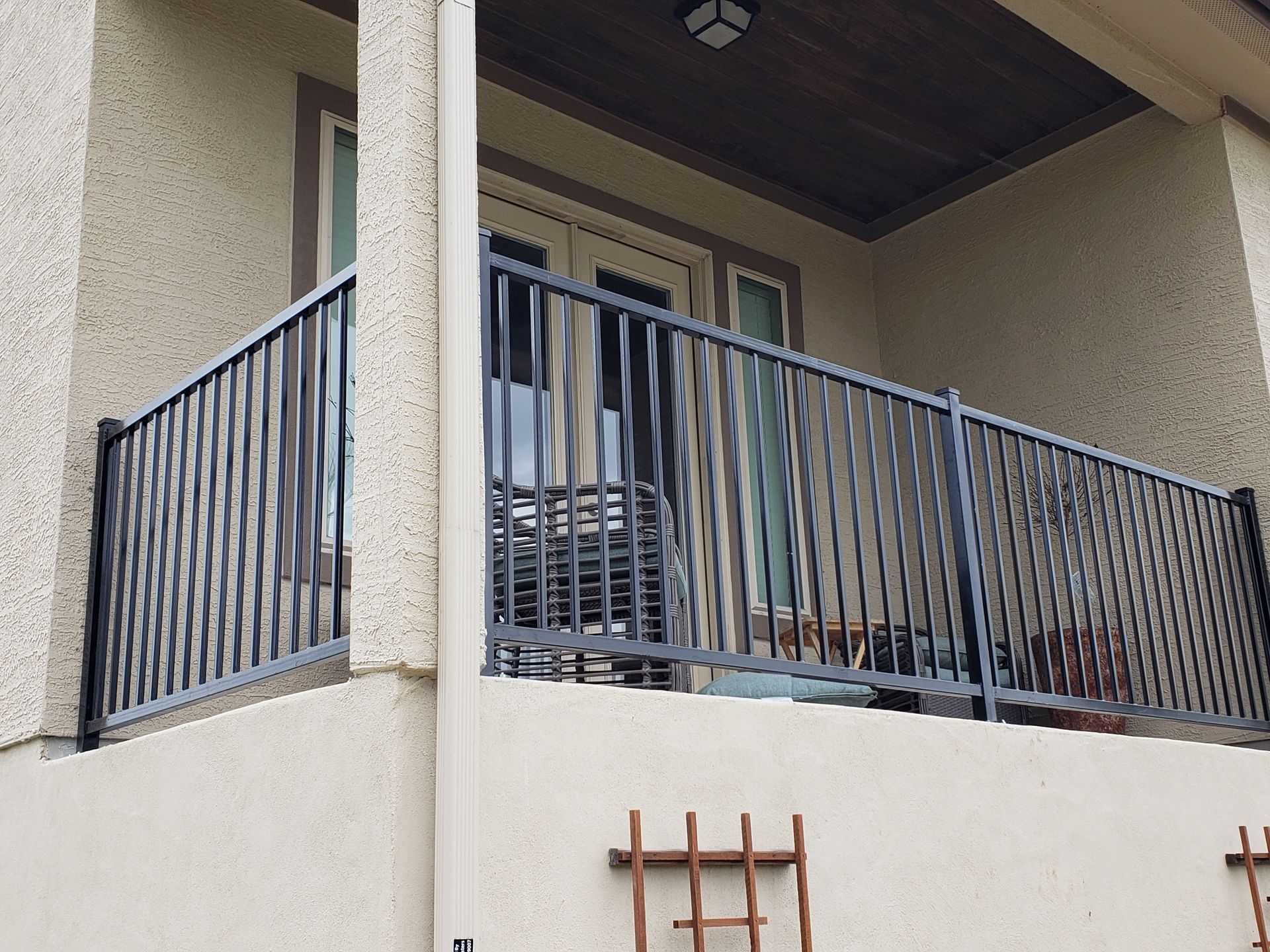 Apartment balcony with black metal railings and a sliding glass door under a covered overhang