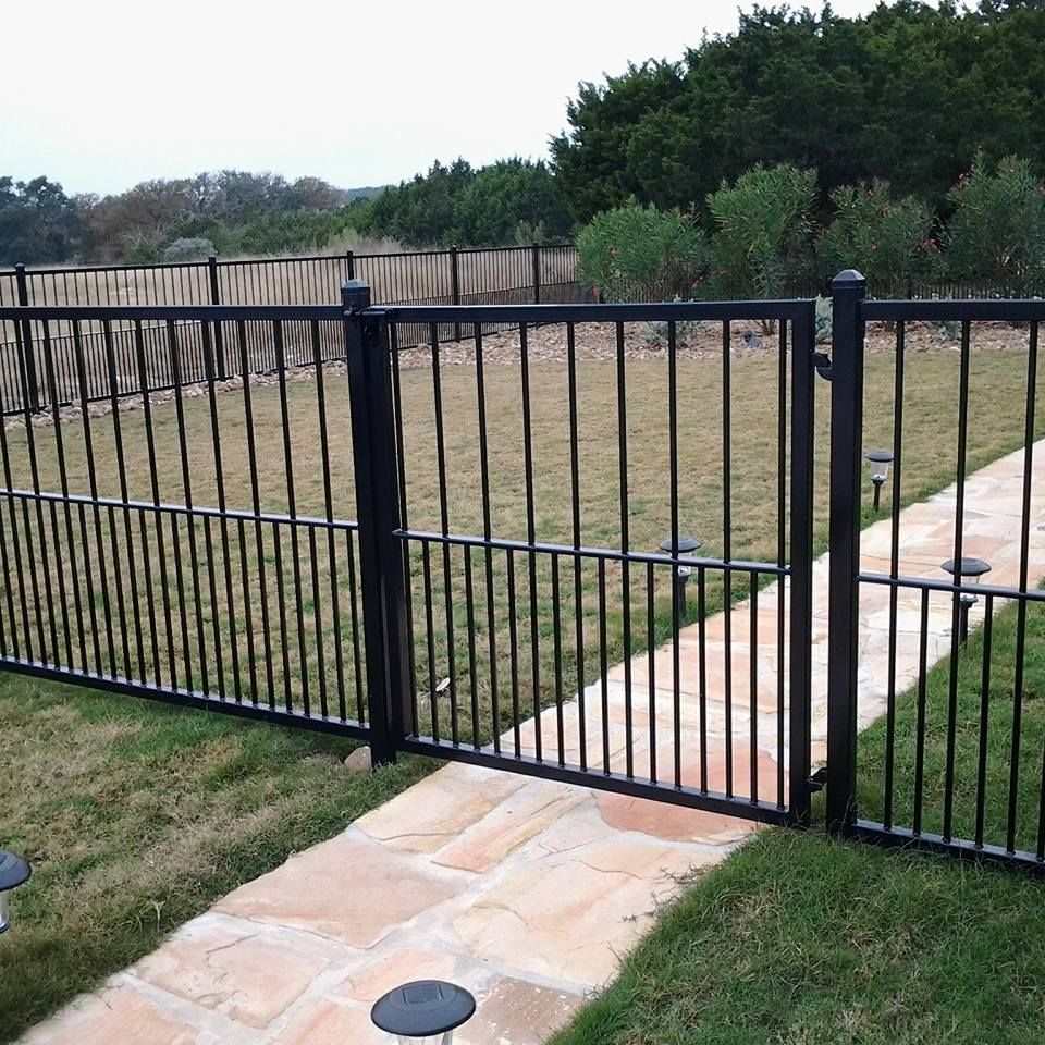 Black metal fence bordering a grassy yard with a stone walkway and gate opening