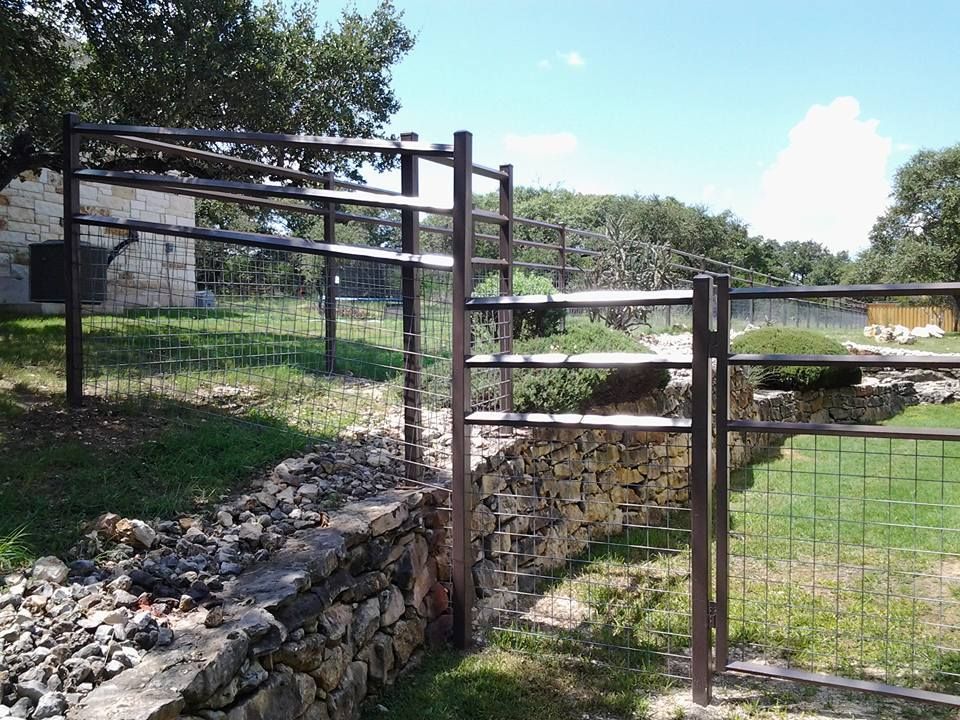 Stone and wire fencing along a grassy path in a sunny park, with trees and a small stream in the background
