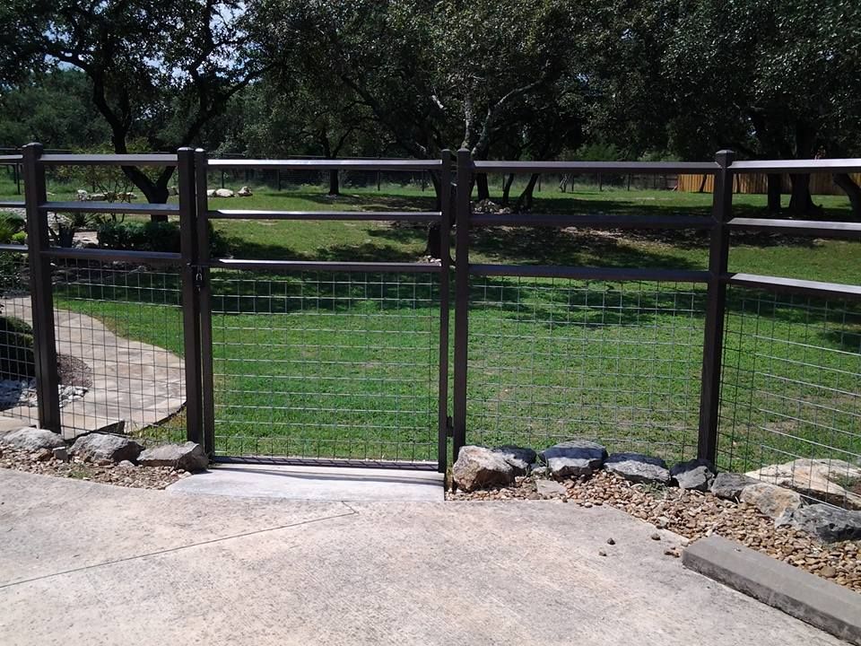 Wooden fence and gate with green mesh around a grassy yard beside a concrete path