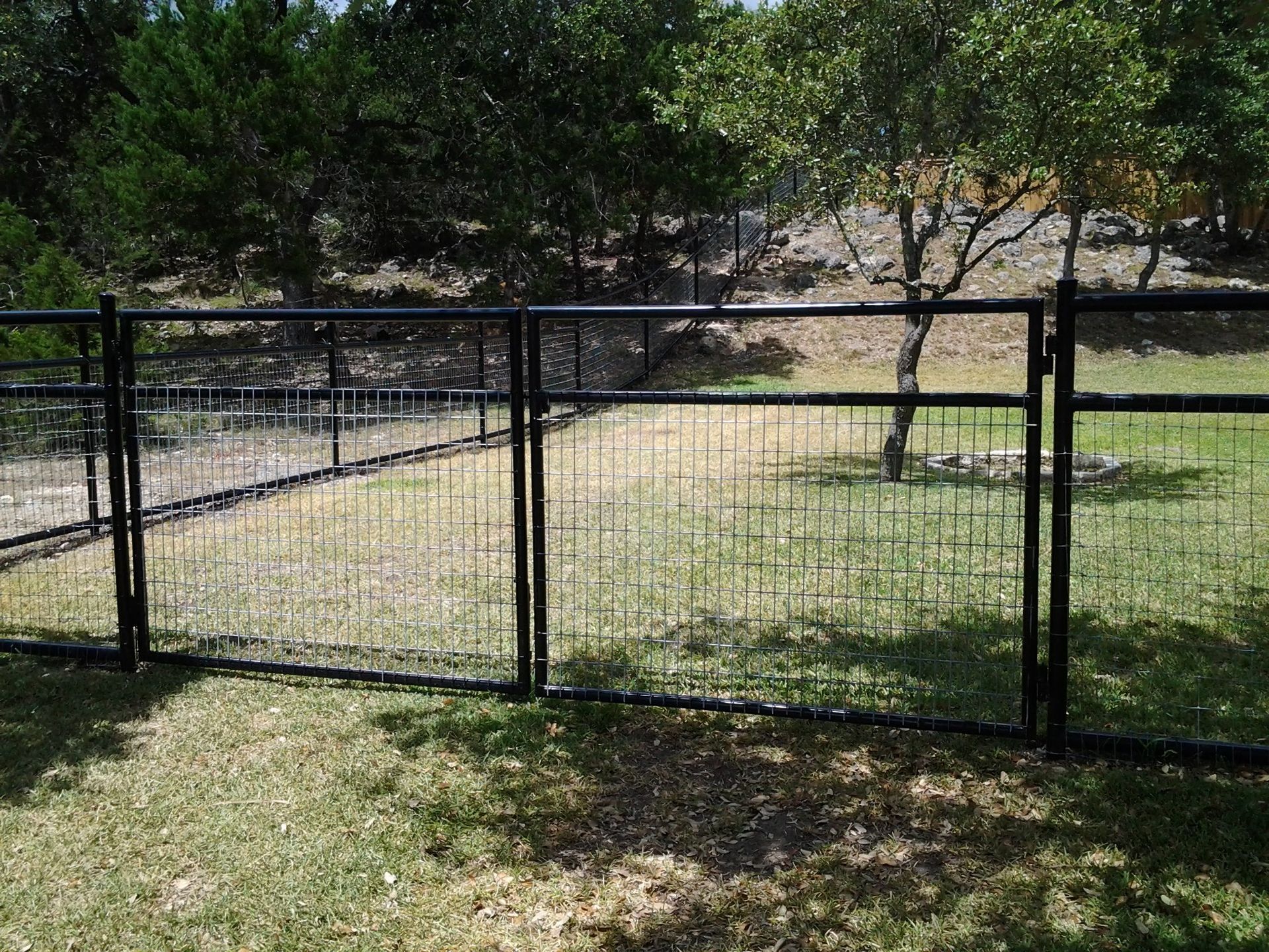 Black metal fence enclosing a grassy yard with trees in the background