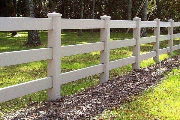 White wooden fence along a grassy path in a wooded area