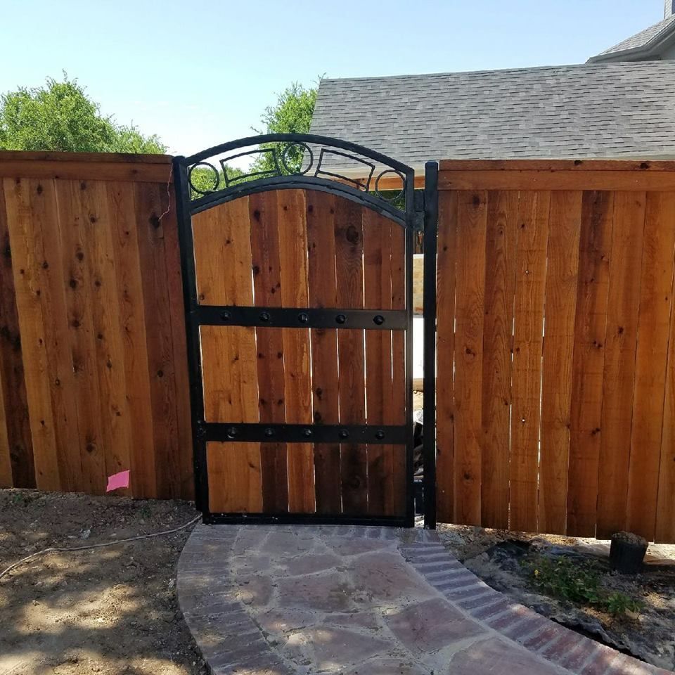 Wooden garden gate with black metal frame set in a wooden fence beside a curved stone path.