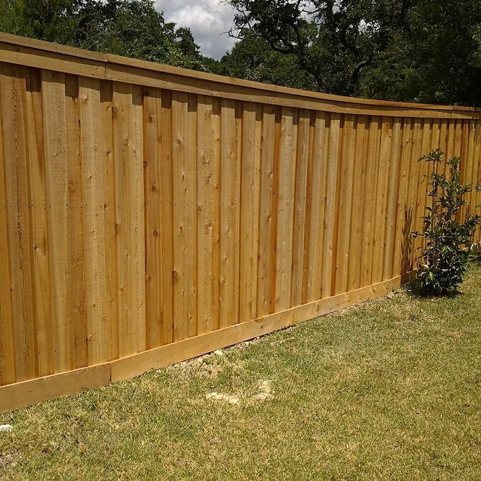 New wooden privacy fence along a grassy yard with trees in the background