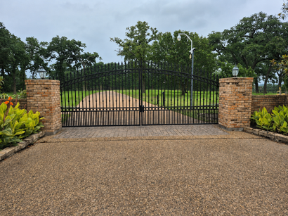 Black iron gate between brick pillars at the entrance to a tree-lined property