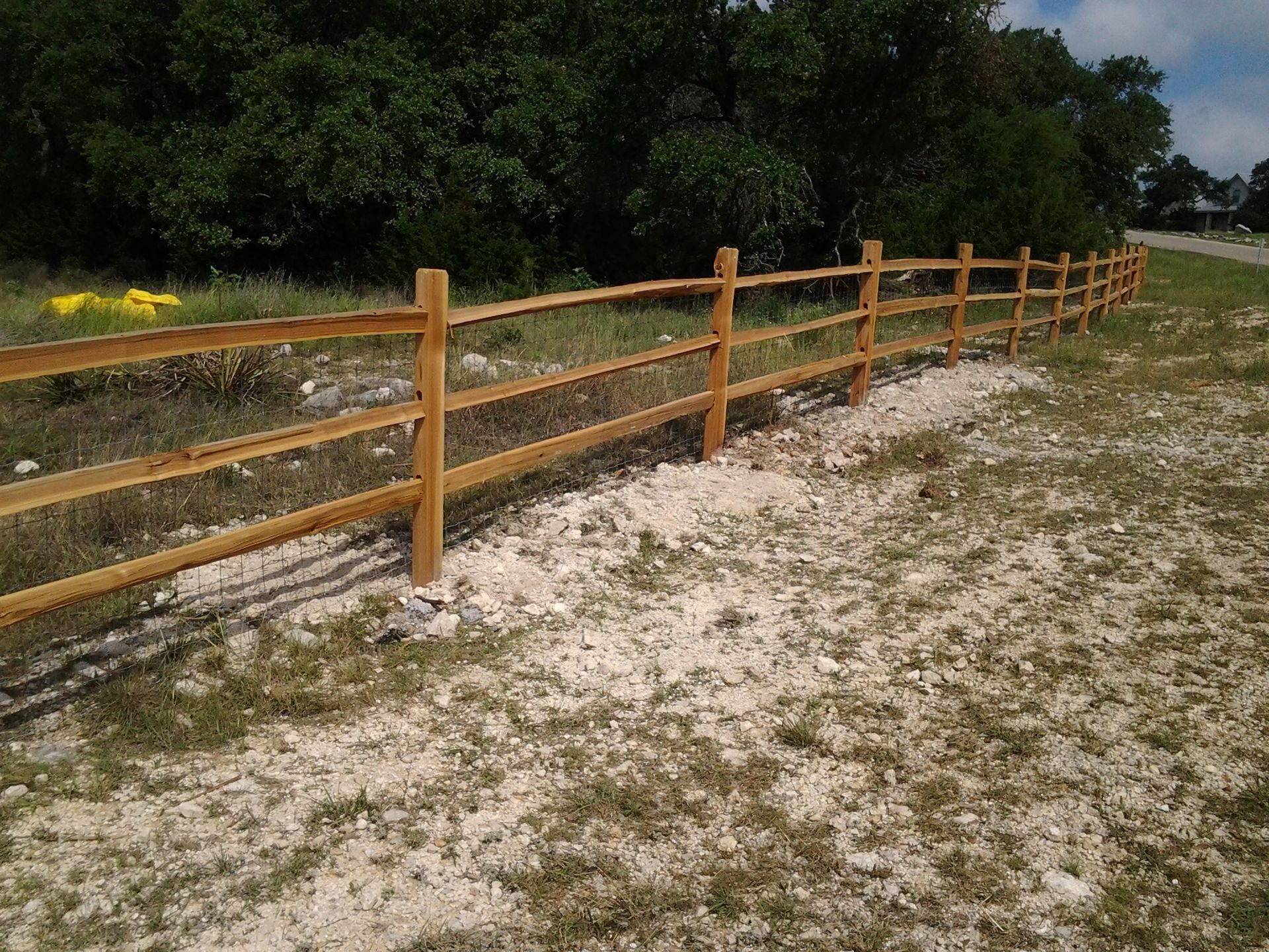 Wooden fence along a sandy path beside a grassy field and trees