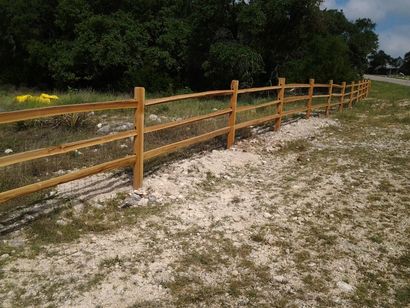 Wooden fence along a sandy path beside a grassy field and trees