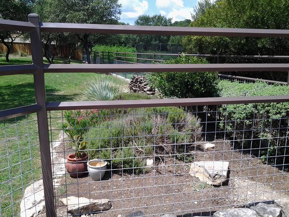 Fenced garden with potted plants, white buckets, and a grassy yard under a blue sky