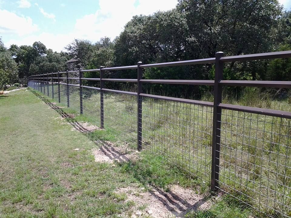 Wire fence running along a grassy path beside trees under a bright sky