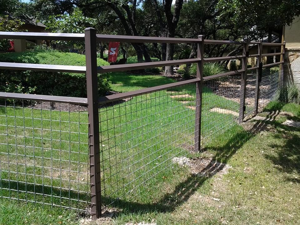 Wire fence gate beside a grassy path in a sunny park with trees and a metal railing
