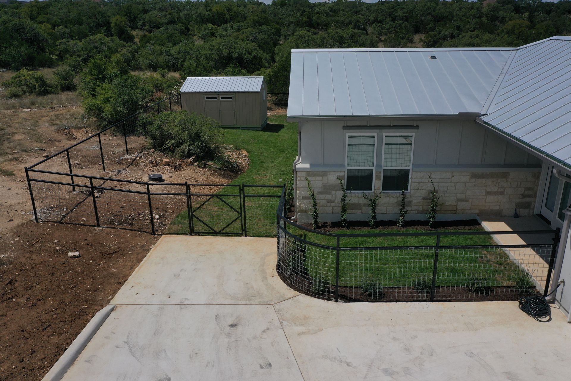 Backyard with a concrete driveway, metal fence, and a gray house with a metal roof.