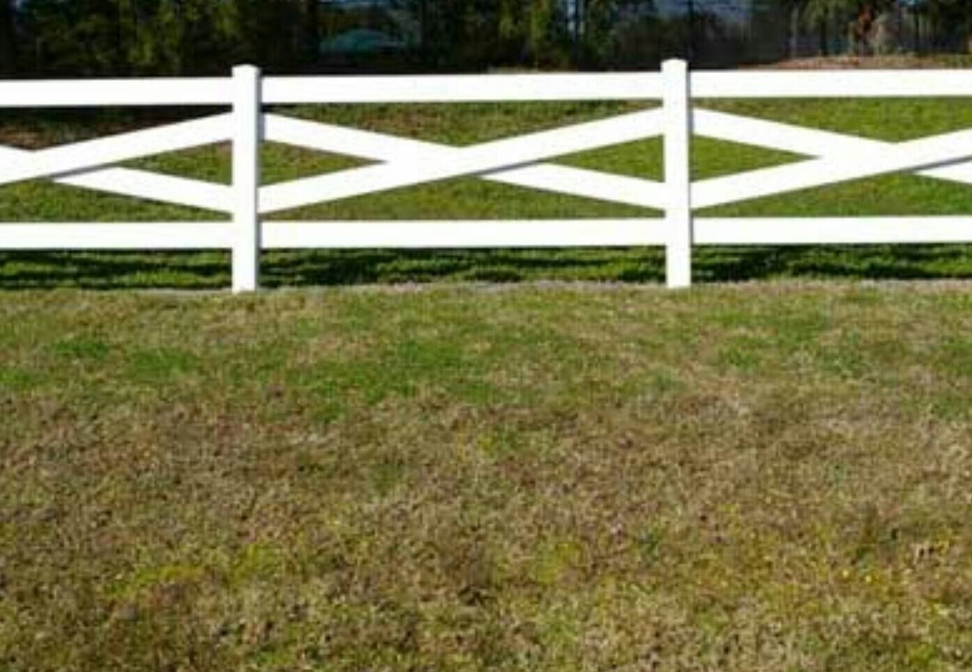 White wooden fence across a grassy field with green trees in the background