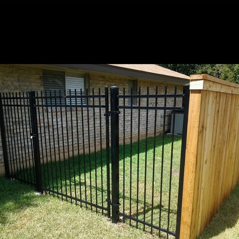Black metal fence beside a wooden privacy fence around a grassy backyard near a brick house