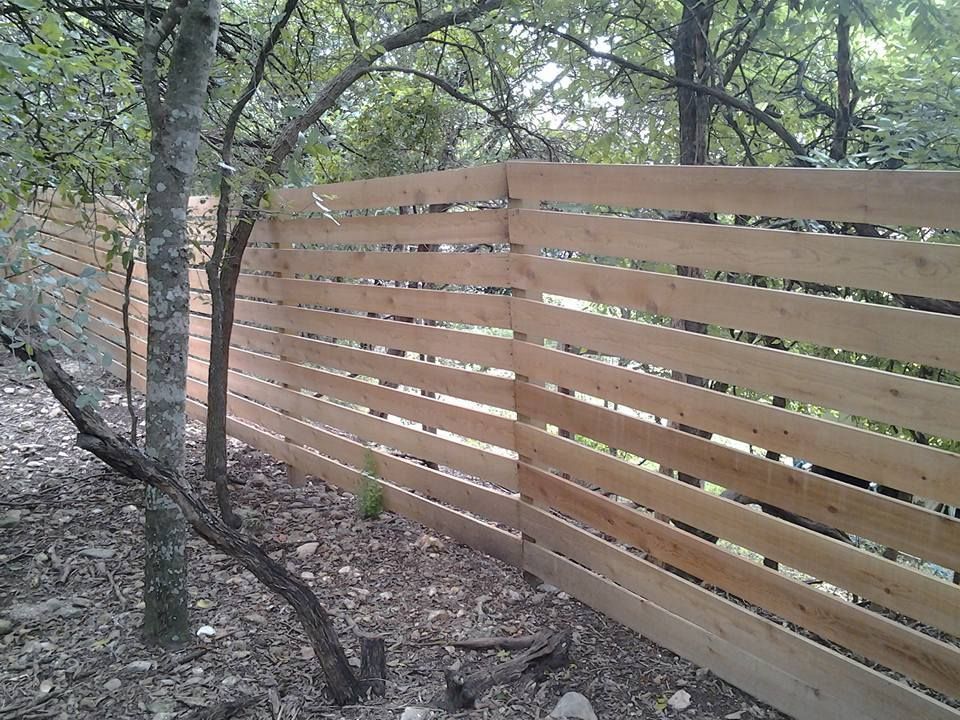 Wooden slat fence in a wooded area with trees and leaf-covered ground