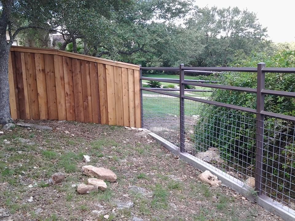 Wooden privacy fence beside a metal gate and railing along a grassy slope.