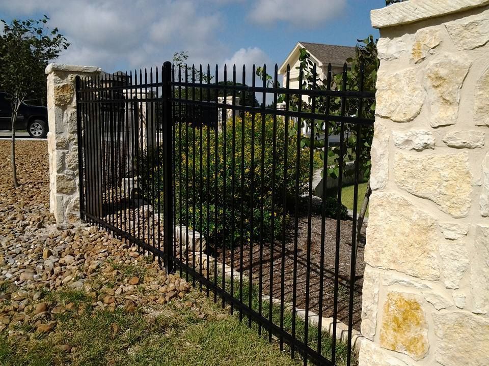 Black metal fence with stone pillars beside a landscaped walkway and house exterior