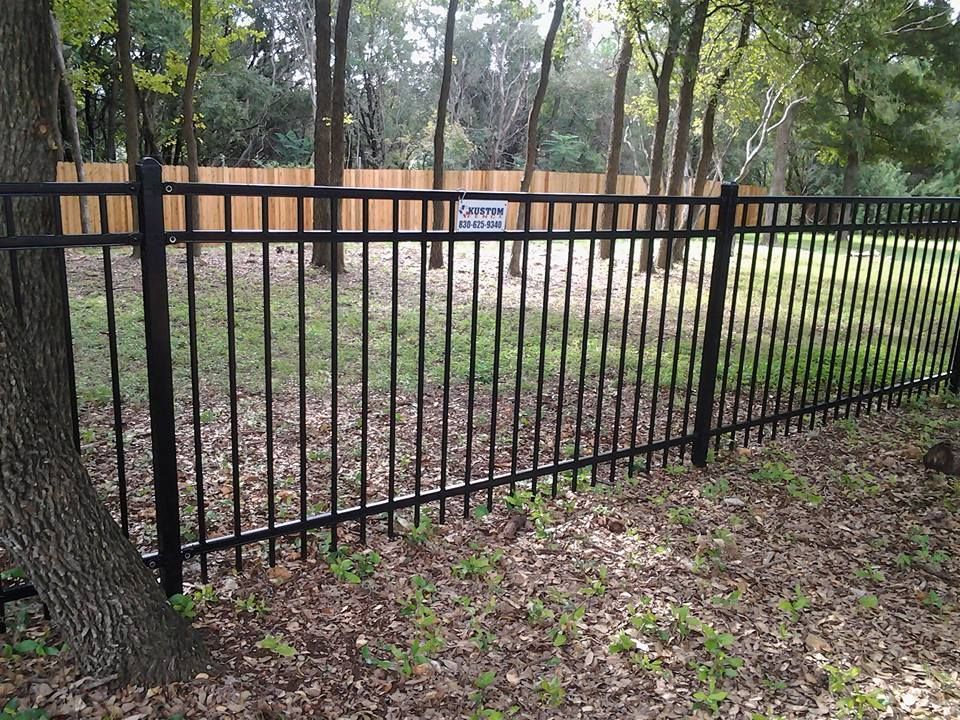 Black metal fence around a wooded area with a small sign and trees in the background