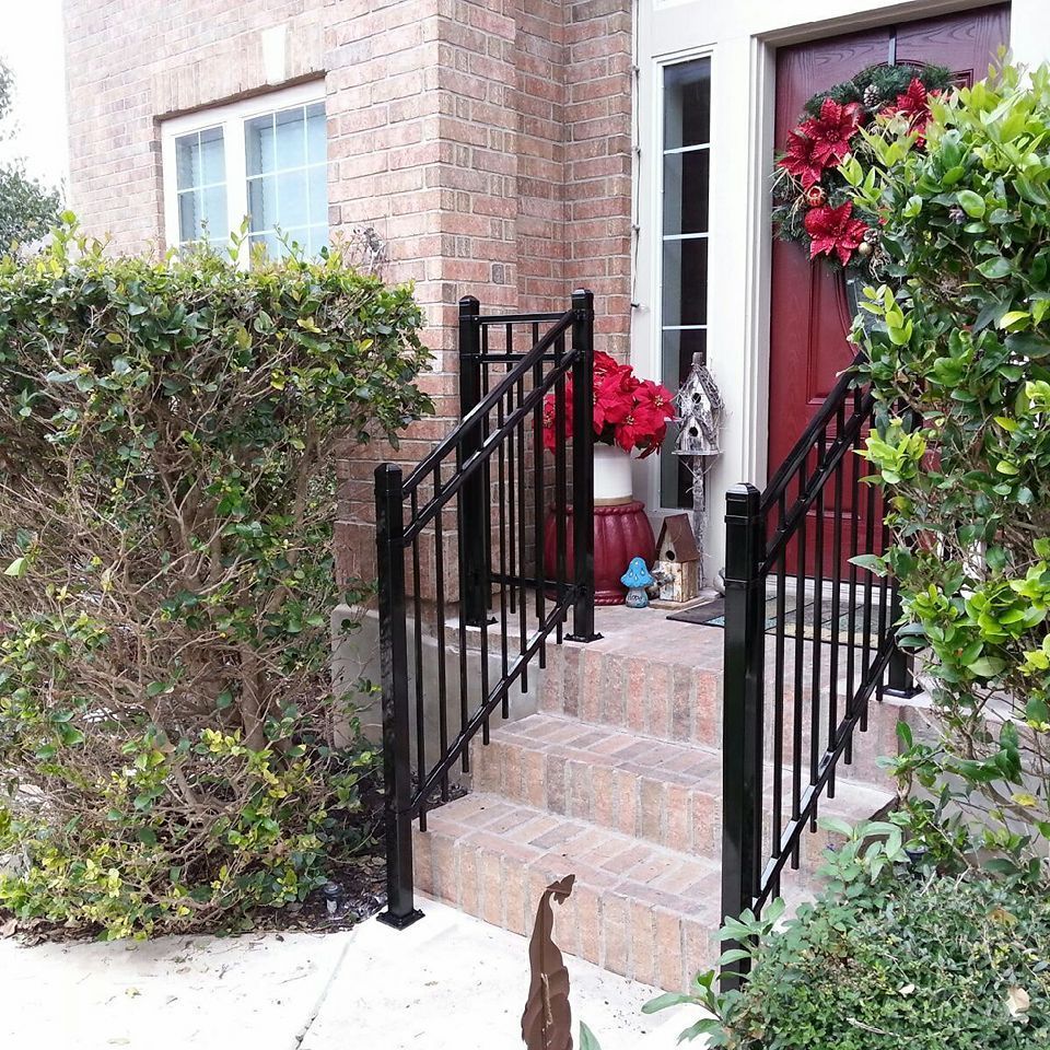 Front porch with black railings, brick steps, and red flowers beside a house entrance.