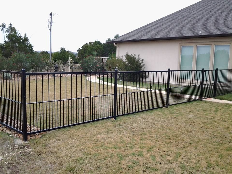 Black metal fence around a beige house and grassy yard under an overcast sky