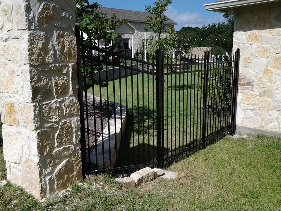 Black wrought-iron gate between stone pillars beside a grassy yard and house