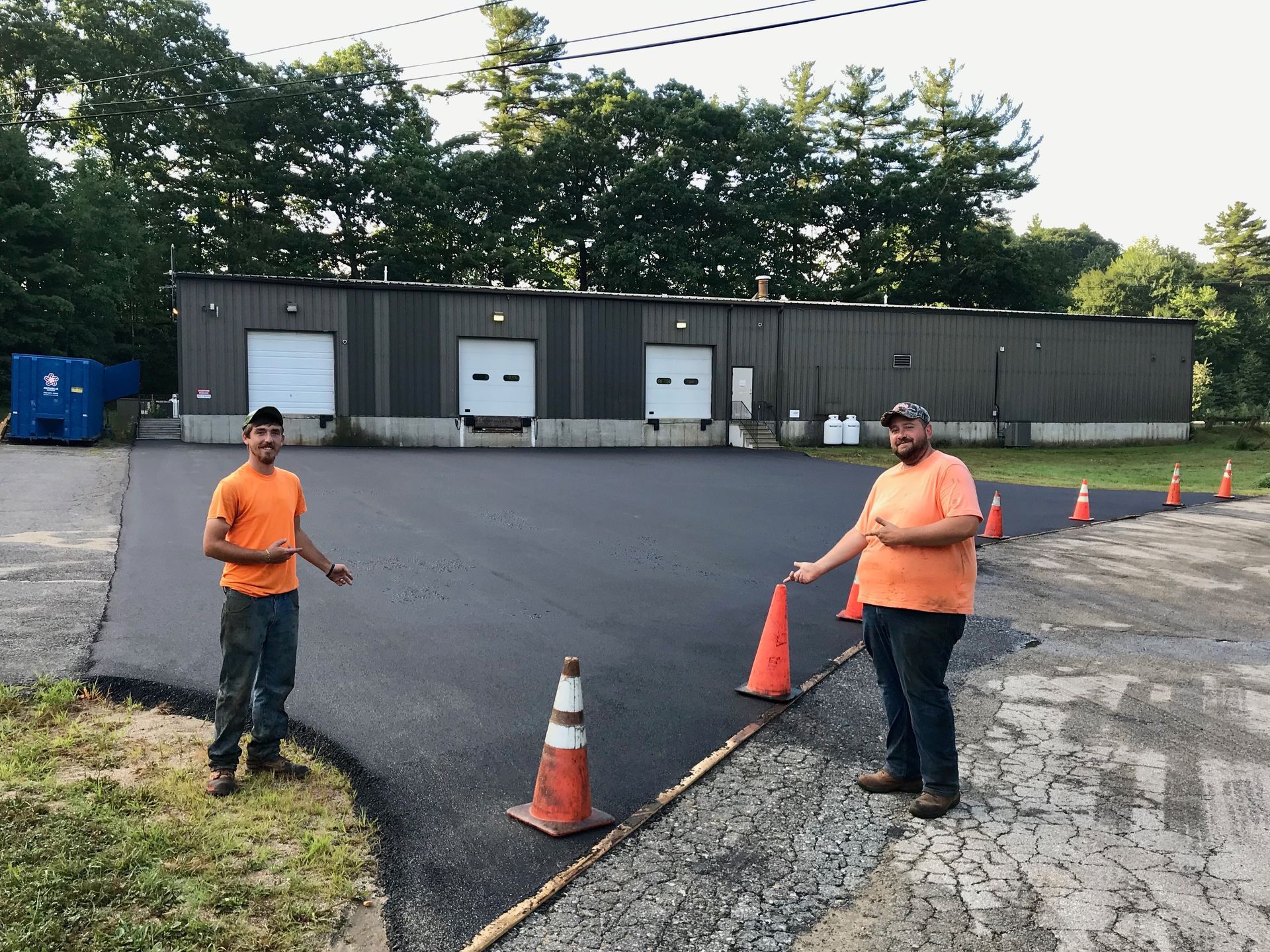 Two men are standing in a parking lot with cones in front of a building.
