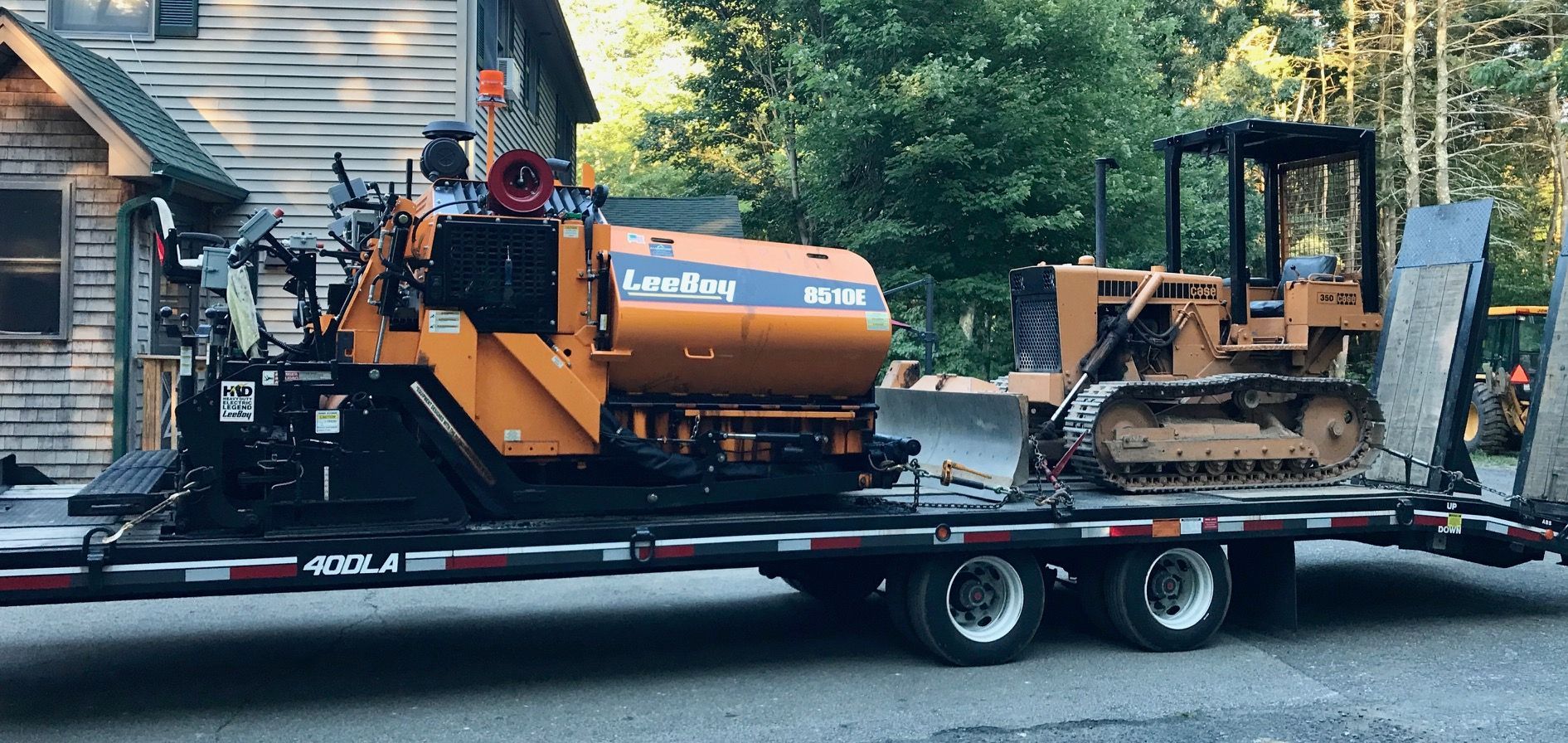 A trailer with a bulldozer on it is parked in front of a house.