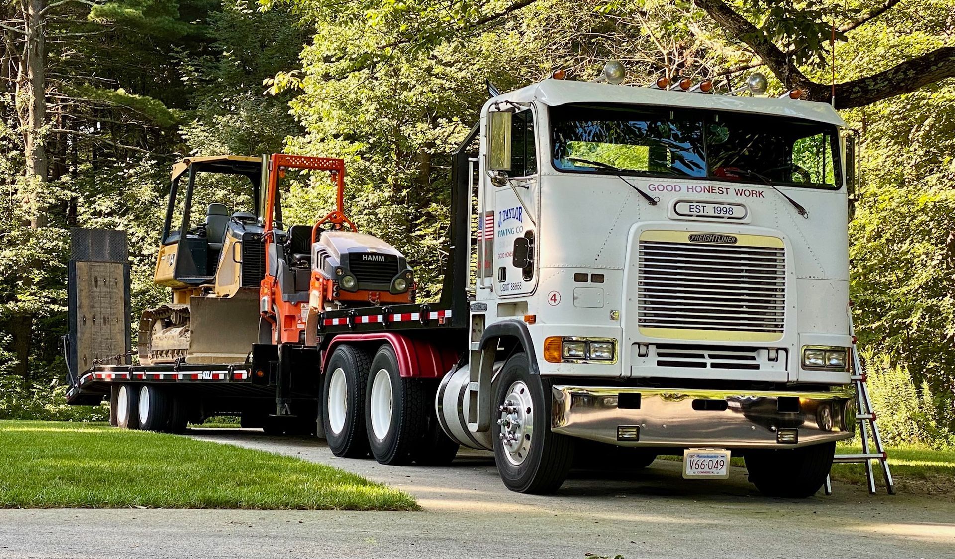 A white semi truck is parked next to a trailer with a bulldozer on it.