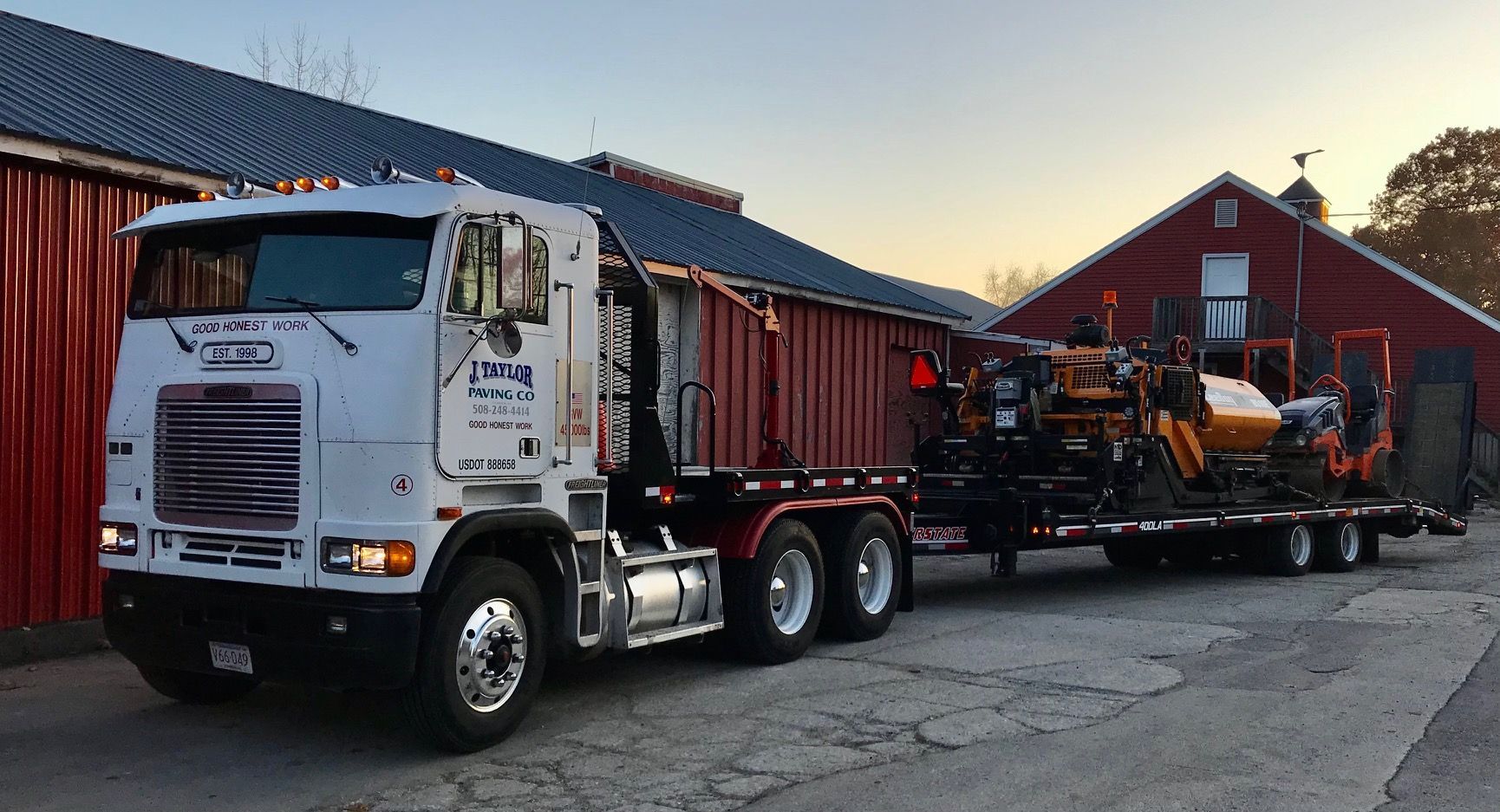 A white semi truck is parked in front of a red barn.