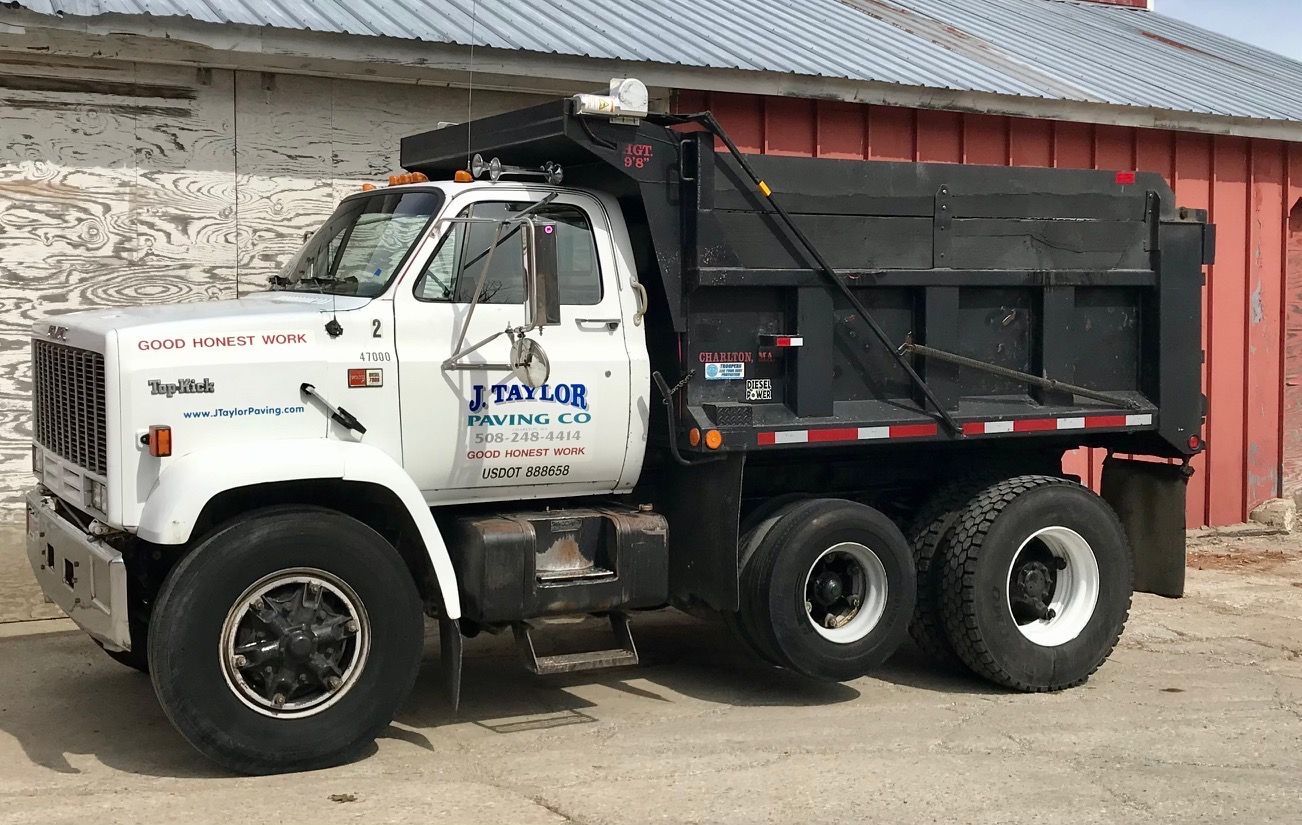 A dump truck is parked in front of a red barn.