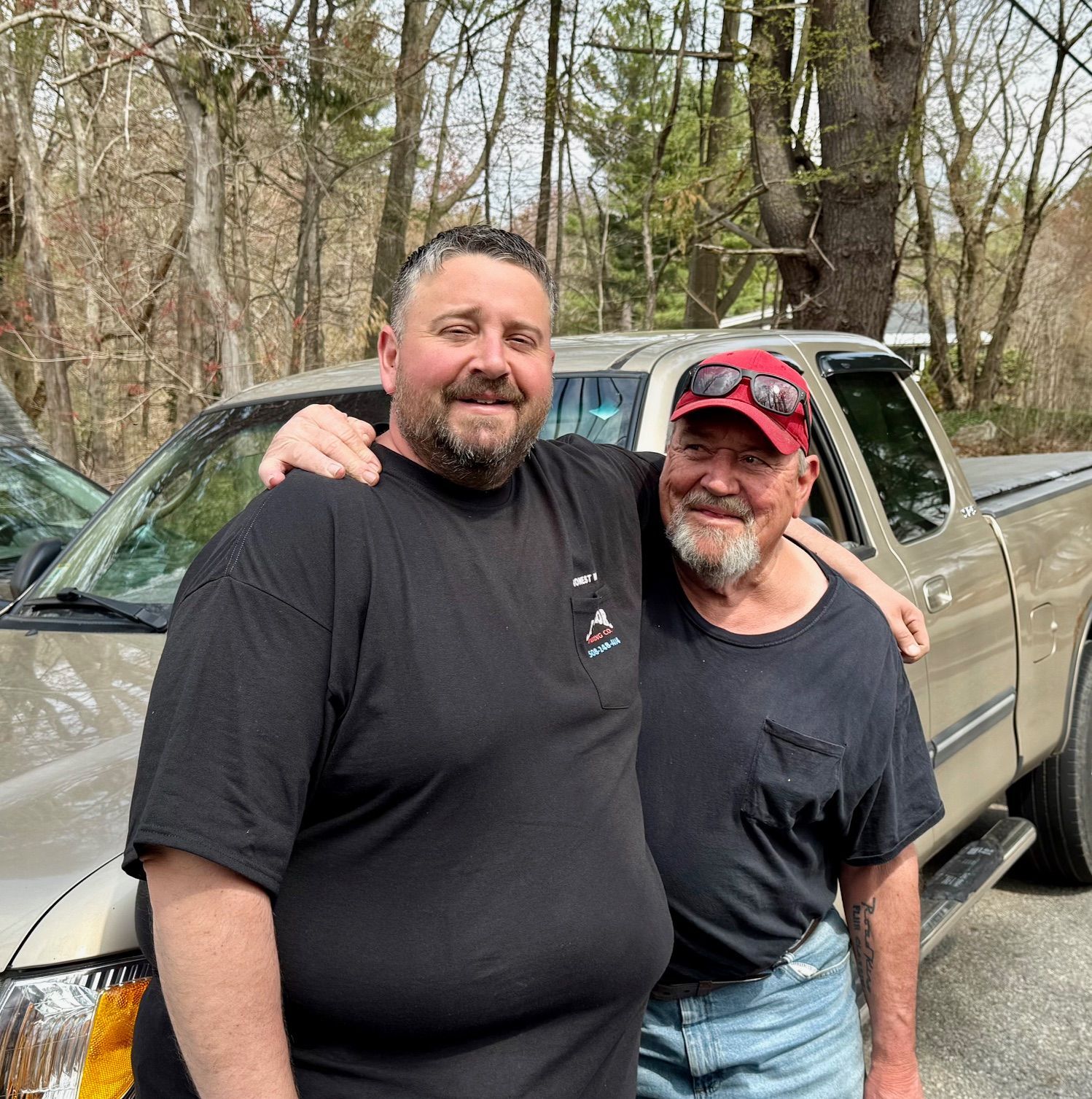 Two men are posing for a picture in front of a truck.