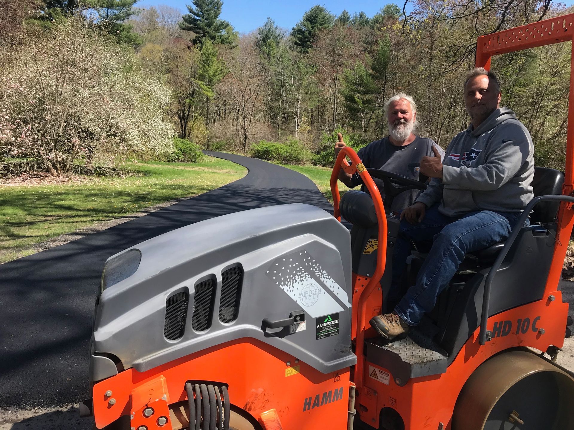 Two men are sitting on a roller on a road.