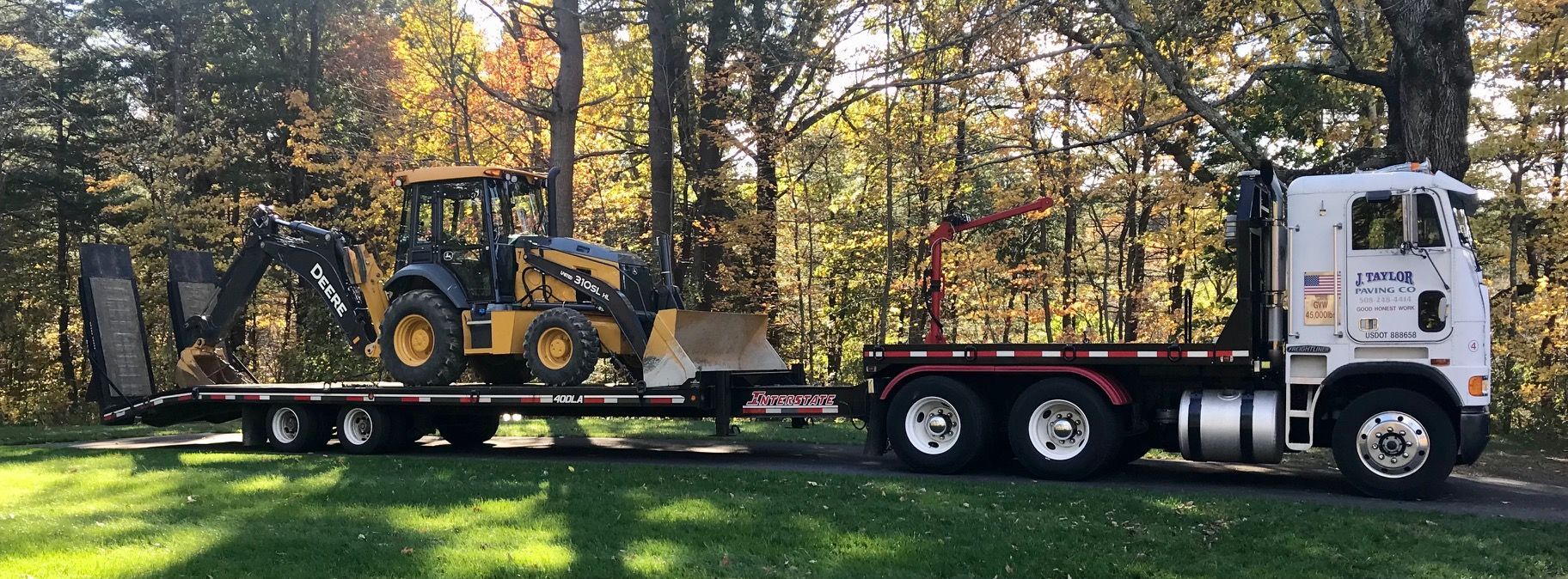 A white truck is carrying a yellow tractor on a flatbed trailer.