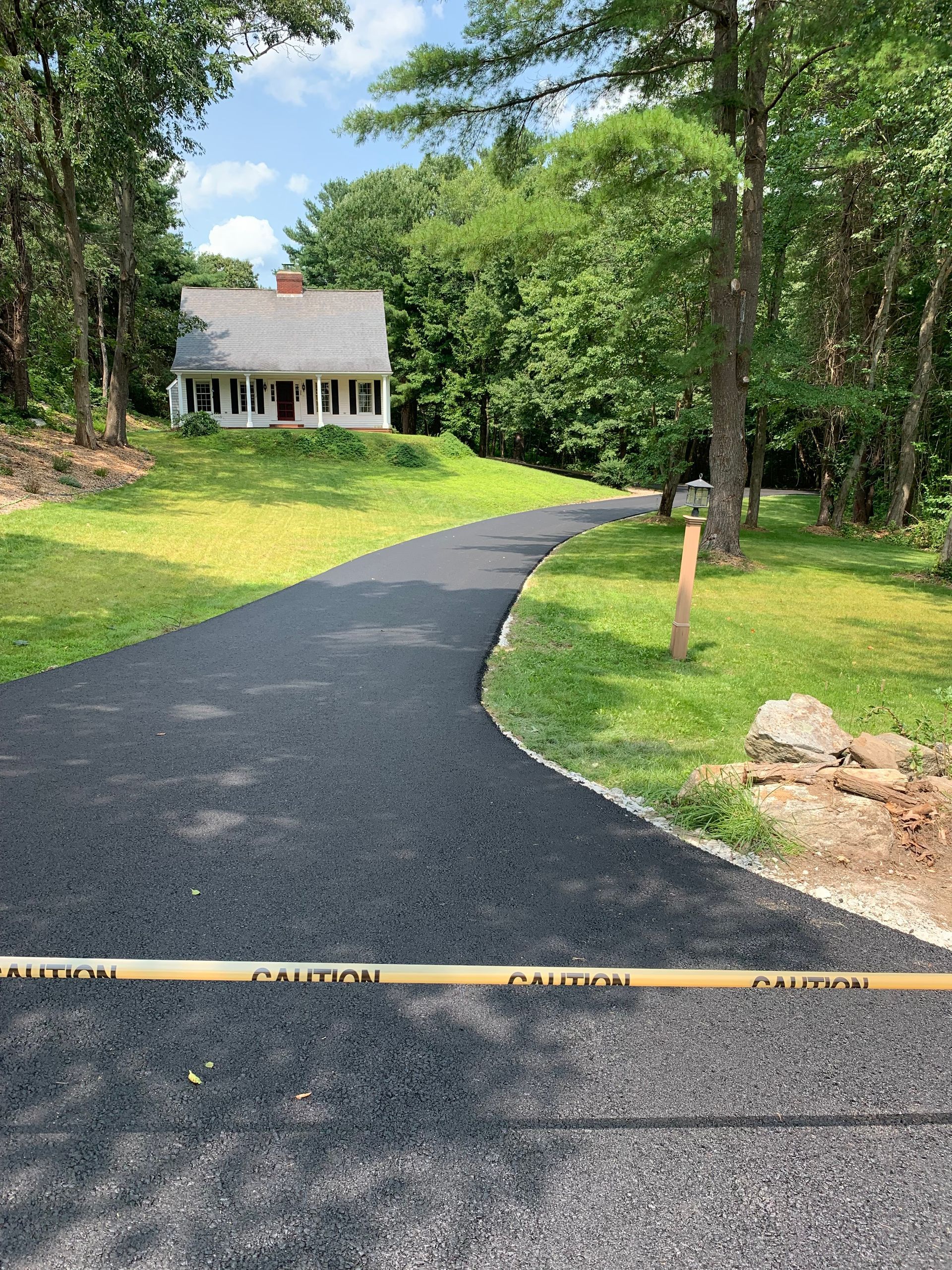 A driveway leading to a house surrounded by trees and grass.