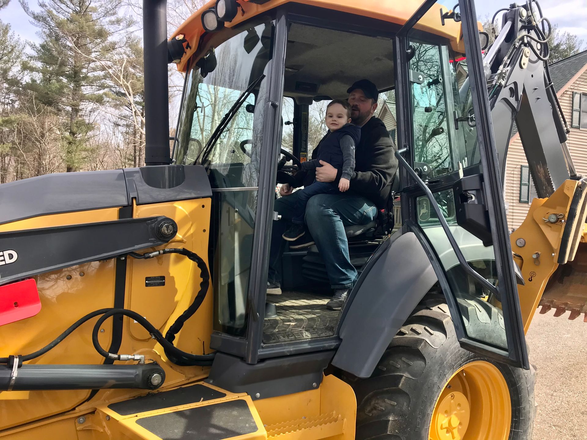 A man and a child are sitting in a yellow tractor.