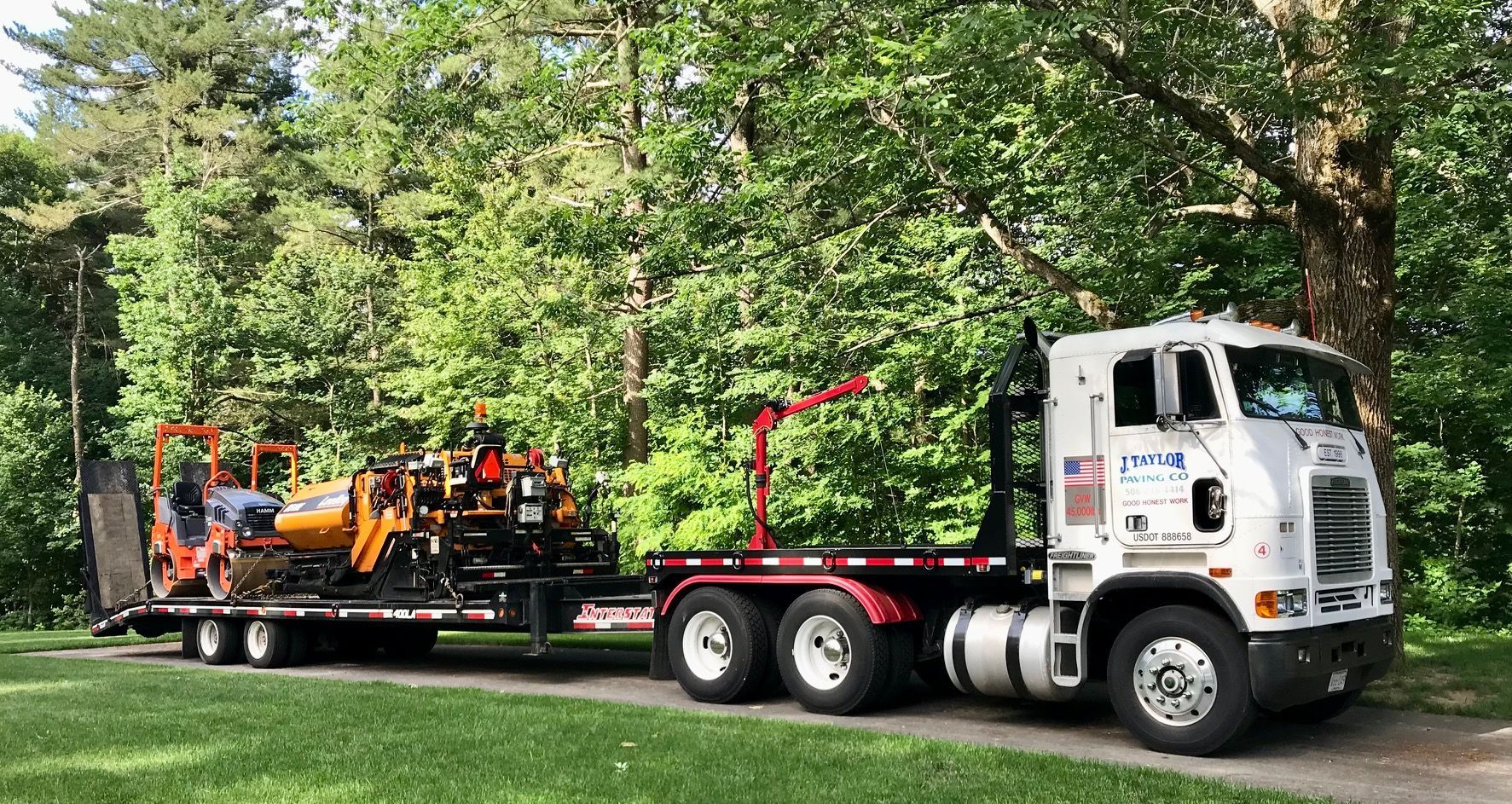 A man is driving an orange asphalt plow in front of a red barn.