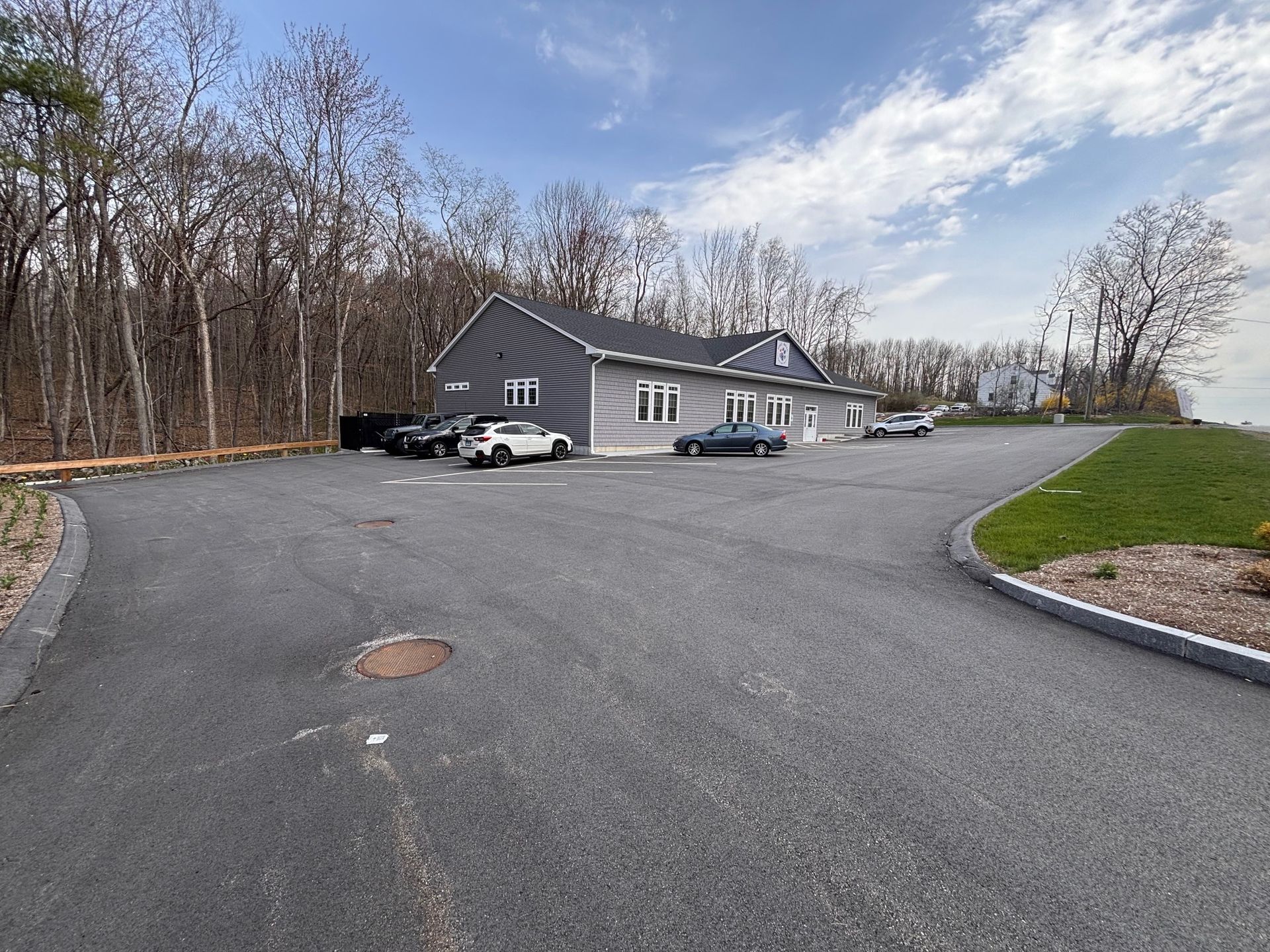 A parking lot with cars parked in front of a house in the woods.