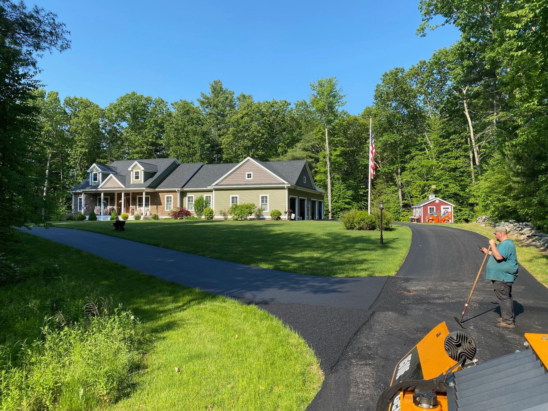 A man is using a snow blower to clear a driveway in front of a house.