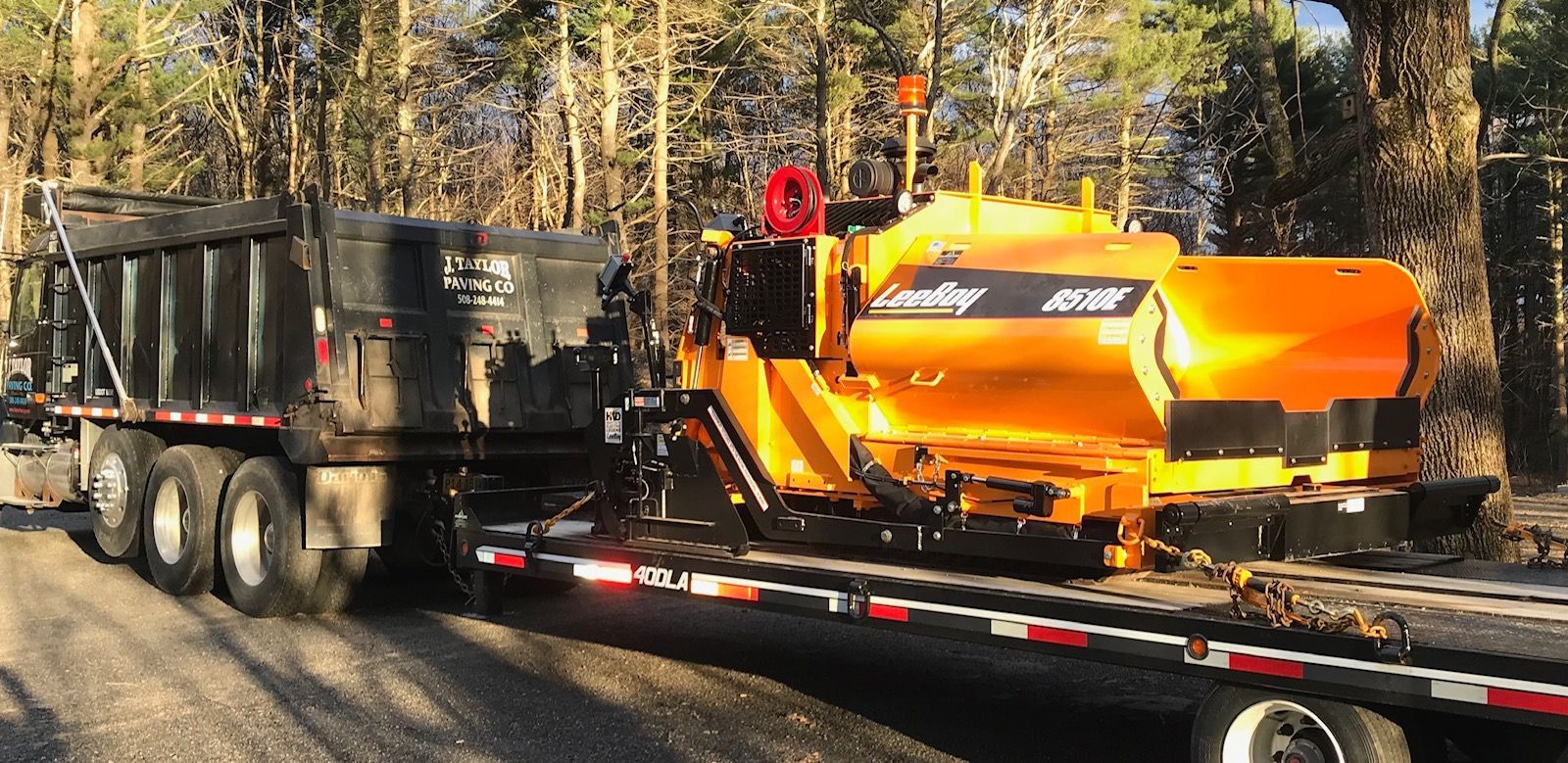A yellow truck with a dump truck attached to it is driving down a dirt road.