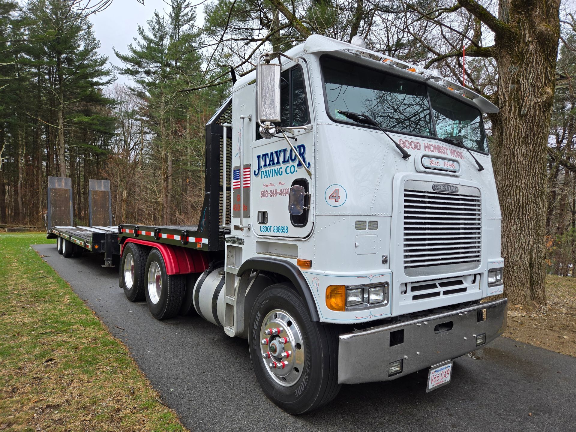 A white semi truck with a flatbed trailer is parked on the side of the road.