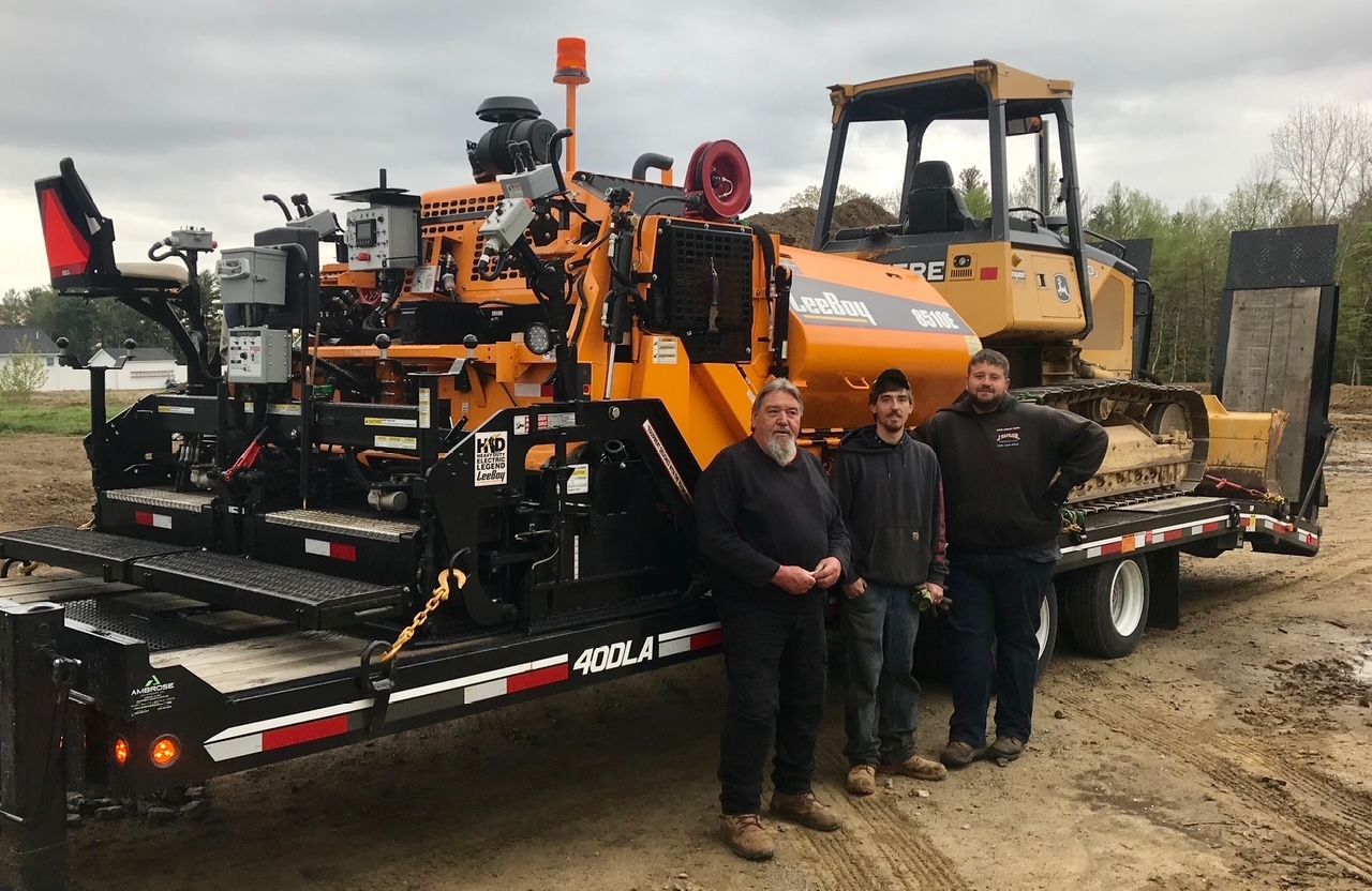 Three men are standing in front of a trailer with a bulldozer on it.