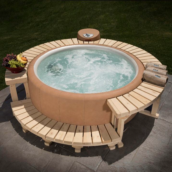 Round inflatable hot tub with wooden surround, on a patio, with fruit and towels.