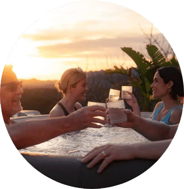 People toasting drinks in a hot tub at sunset.