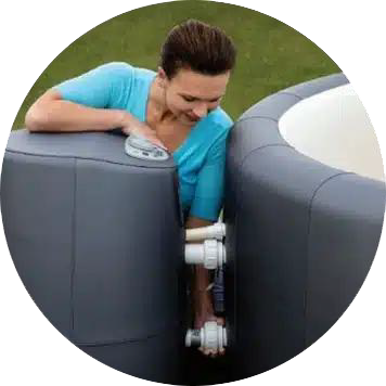 Woman installing equipment on a dark gray inflatable hot tub in an outdoor setting.