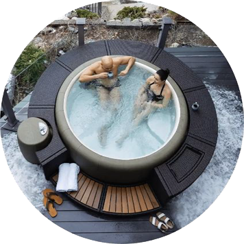 Couple relaxing in an outdoor hot tub with drinks, surrounded by dark wooden decking and stone.