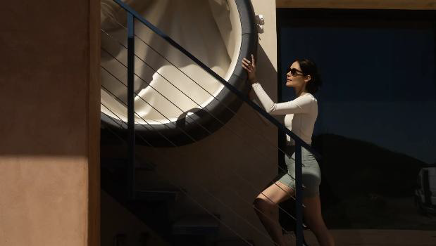 Woman in sunglasses climbs stairs near a large, circular architectural feature.