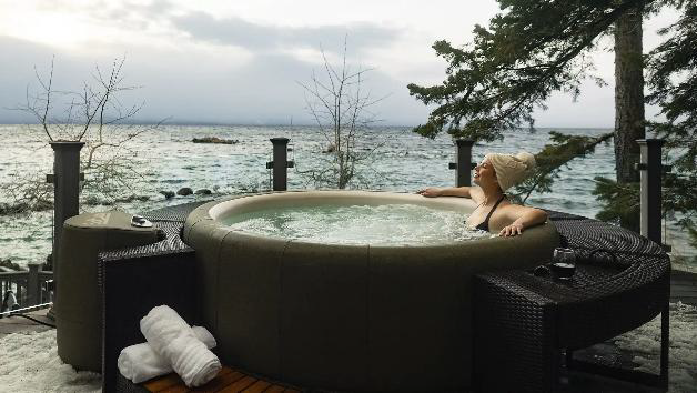 Woman relaxing in a hot tub overlooking a lake on a cloudy day.