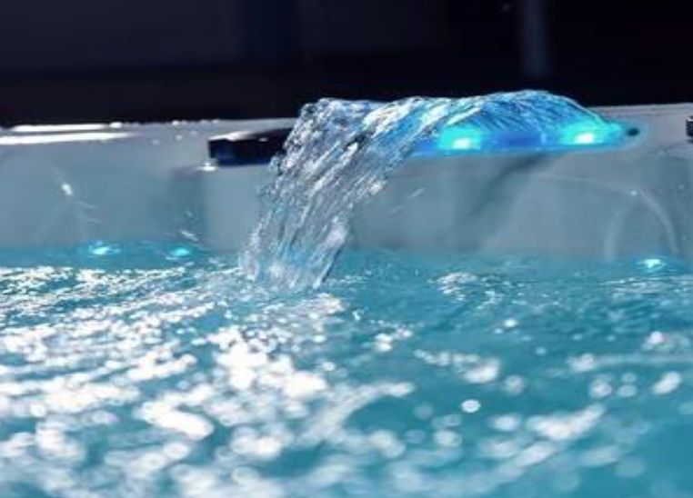 Close-up of a hot tub with water cascading from a lighted feature into the clear, rippling water.
