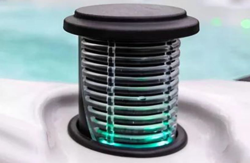 Black, cylindrical spa speaker with glowing green light, set in a white spa.