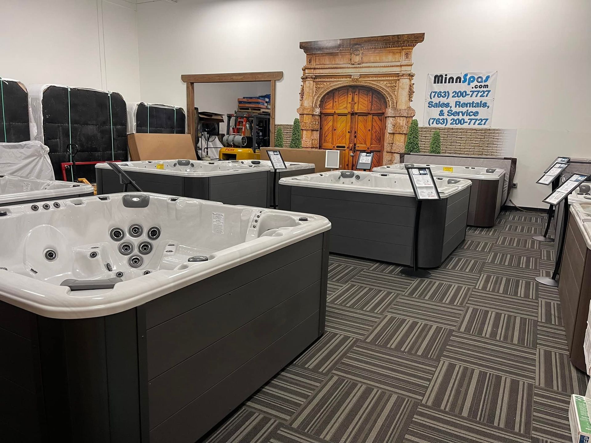 Hot tubs displayed in a showroom with a decorative backdrop and patterned carpet.
