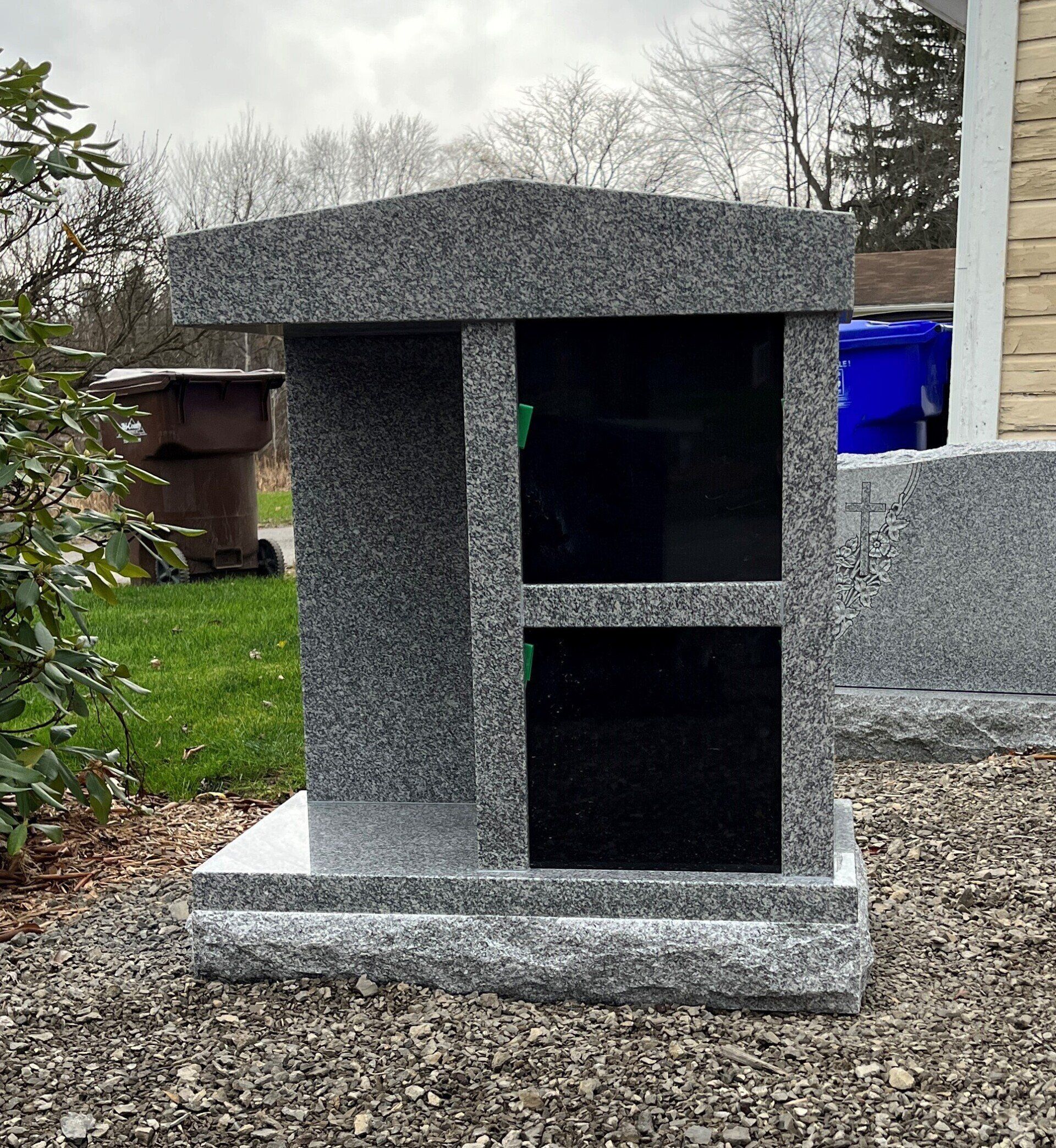 A small granite memorial is sitting on top of a gravel lot in front of a house.